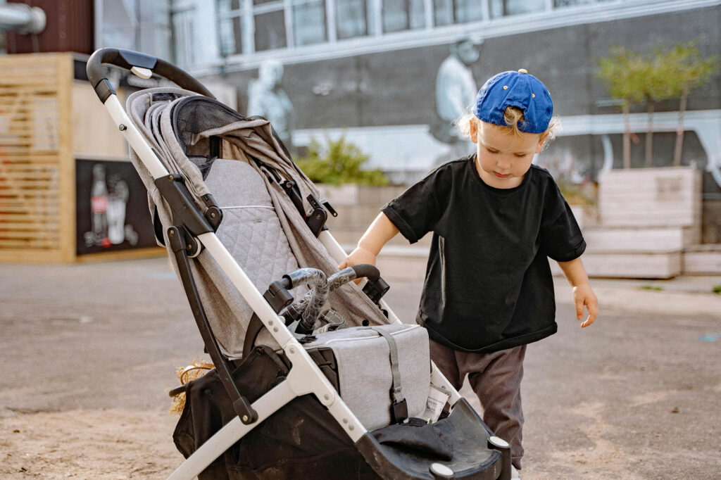 A photo of a toddler stood next to a pushchair